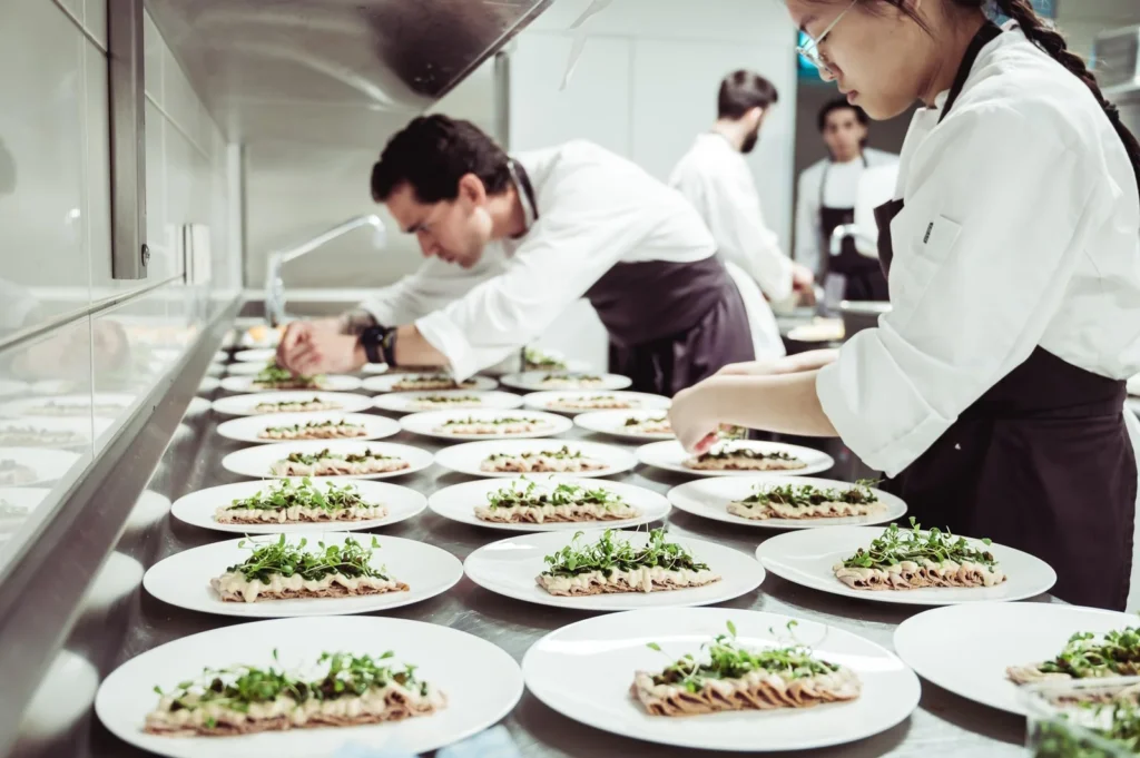 Restaurant kitchen staff plating dishes consistently using standard recipes