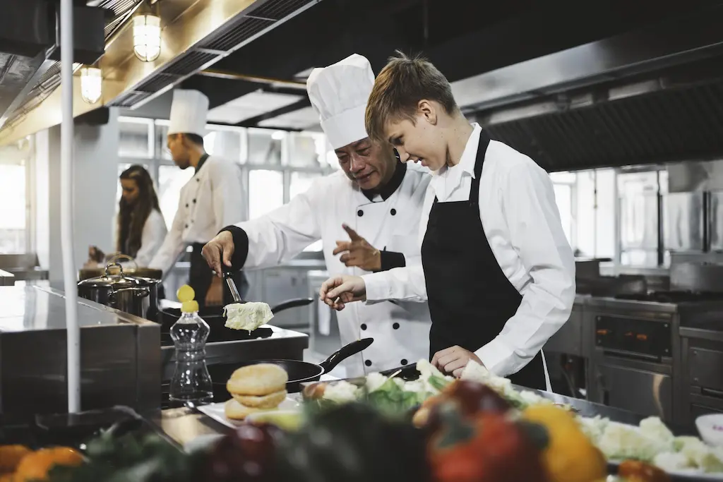 Experienced restaurant employee teaching accurate measuring to a new kitchen worker